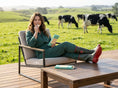Load image into Gallery viewer, Woman sitting on a chair in a paddock with cows, holding a wayne raven chocoate.
