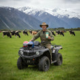 Load image into Gallery viewer, A happy dairy farmer on a quad bike holding Wayne Raven's white chocolate bar in an alpine setting
